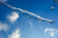 A semi-melted transparent icicle lies on a pane of glass against a blue sky background with small white clouds. Icy Ice rain drop