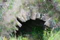 Semicircular stone entrance to the cave grotto, sunny summer day, grass, wild flowers