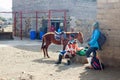 Lesotho, young african shepherd man in national woolen blanket dress sits on big stone with friend and horse on rural town street