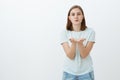 Sending sweet kiss by air. Portrait of charming carefree cute woman in trendy t-shirt bending towards camera with palms