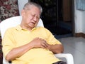 Senile asian men sitting on a chair at living room with heart attacks.Both old man`s hands on breast because of hard breathing Royalty Free Stock Photo