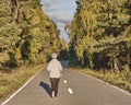 Senior active woman with gray hair running along forest paved road on sunny autumn day. Royalty Free Stock Photo