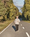 Senior active woman with gray hair running along forest paved road on sunny autumn day. Royalty Free Stock Photo