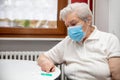 Senior adult elderly woman with grey hair and a mask and a vaccination syringe on the table