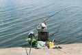 Senior adult man on river bank casting the fishrod. Fishman is sitting in the chair surrounded by fishing equipment. Color image