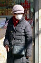 A senior adult woman stands on a street corner with a mask