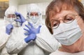 Senior Adult Woman Wearing Medical Face Mask In Doctor Office With Nurses In HAZMAT Suits Behind Royalty Free Stock Photo