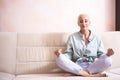 Senior Adults and Yoga Concepts. Portrait of Relaxing Caucasian Senior Woman Posing in Yoga Asana Pose on Couch indoors. Sitting