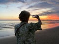 Senior adventure is ageless woman with a mobile phone take a photo of beautiful of sunset near sea beach. Summer vacation for