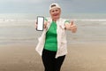 Senior adventure is ageless woman with a mobile phone with white blank for your ads on the sea beach near old center of Antalya.