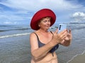 Senior adventure is ageless woman wearing in swimsuit speak by mobile phone on the beach. Summer vacation for pensioner
