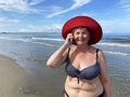 Senior adventure is ageless woman wearing in swimsuit speak by mobile phone on the beach. Summer vacation for pensioner