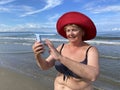 Senior adventure is ageless woman wearing in swimsuit speak by mobile phone on the beach. Summer vacation for pensioner