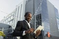 A senior African American businessman is talking to his team via video call. Standing near an office center in a suit Royalty Free Stock Photo