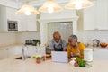 Senior african american couple cooking together in kitchen using laptop Royalty Free Stock Photo
