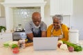 Senior african american couple cooking together in kitchen using laptop Royalty Free Stock Photo