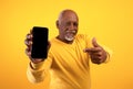 Senior African American man pointing at mobile phone with empty screen over orange studio background, mockup Royalty Free Stock Photo