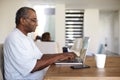 Senior African American  man sitting at the table using a laptop computer at home, side view Royalty Free Stock Photo