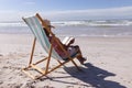 Senior african american woman reading a book while sitting on deck chair at the beach Royalty Free Stock Photo