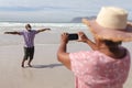 Senior african american woman taking a picture of her husband on the beach Royalty Free Stock Photo