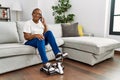 Senior african american woman talking on the smartphone and doing sport using bike pedals machine at home