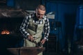 Senior an artisan blacksmith knocks with a hammer on iron to shape against the background of a burning forge Royalty Free Stock Photo