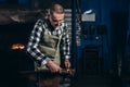Senior an artisan blacksmith knocks with a hammer on iron to shape against the background of a burning forge Royalty Free Stock Photo