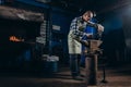 Senior an artisan blacksmith knocks with a hammer on iron to shape against the background of a burning forge Royalty Free Stock Photo