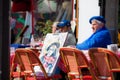 Senior artist with a self portrait sitting at a cafe at the famous Place du Tertre in Montmartre