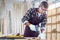 Senior Asian carpenter wear safety glasses and cloth gloves in woodwork workshop, old citizen craftsman work with hand drill in Royalty Free Stock Photo