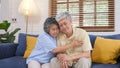 Senior asian couple comforting each other from depressed emotion while sitting on sofa at home living room, old retirement