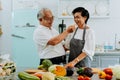 Senior Asian couple grandparents cooking together while woman is feeding food to man at the kitchen. Long lasting Royalty Free Stock Photo