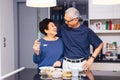 Senior Asian couple grandparents cooking together while woman is feeding food to man at the kitchen Royalty Free Stock Photo