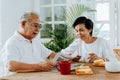 Senior Asian couple having breakfast together in dinner room. 70s retired elderly man and woman reading newspaper Royalty Free Stock Photo