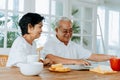 Senior Asian couple having breakfast together in dinner room. 70s retired elderly man and woman reading newspaper Royalty Free Stock Photo