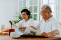 Senior Asian couple having breakfast together in dinner room. 70s retired elderly man reading newspaper while woman Royalty Free Stock Photo