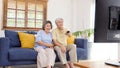 Senior asian couple holding remote control while watching television in home living room with happiness, old people retirement Royalty Free Stock Photo