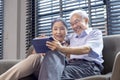 Senior Asian couple in retirement age looking at nostalgic photo using digital tablet while sitting on the sofa couch in their