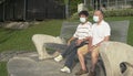 Senior Asian couple wearing face mask sitting on a bench in a park Royalty Free Stock Photo