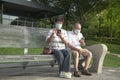 Senior Asian couple wearing face mask, sitting and reading their phones in a park Royalty Free Stock Photo