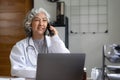 Senior asian female doctor using mobile phone talking while sitting in hospital office. happy woman medical worker Royalty Free Stock Photo