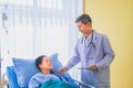 Senior asian male doctor visiting and talking with middle-aged female patient on Ward. Royalty Free Stock Photo