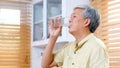 Senior asian man drinking water while standing by window in kitchen background, elderly retirement people and healthy lifestyles Royalty Free Stock Photo