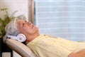 Senior asian man listening headphones whlie laying on sofa in home living room with happiness, retirement lifestyle and technology Royalty Free Stock Photo