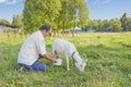 Senior asian man milking white goat on meadow.