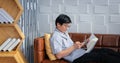 Senior Asian man reading book and using smart phone on sofa in living room at home  Portrait of Asian elderly man is Relaxing and Royalty Free Stock Photo