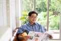 Senior Asian man reading newspaper mock up at the sofa couch inside of the house in the morning. Happy retirement with relaxation Royalty Free Stock Photo