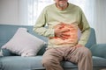 Senior Asian man sitting on sofa having suffering from stomach ache holding his stomach pain Royalty Free Stock Photo