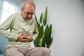 Senior Asian man sitting on sofa having suffering from stomach ache holding his stomach pain Royalty Free Stock Photo