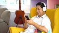 Senior asian man using smartphone   listening music with headphones, sitting on sofa in living room at home, Old male relaxation Royalty Free Stock Photo